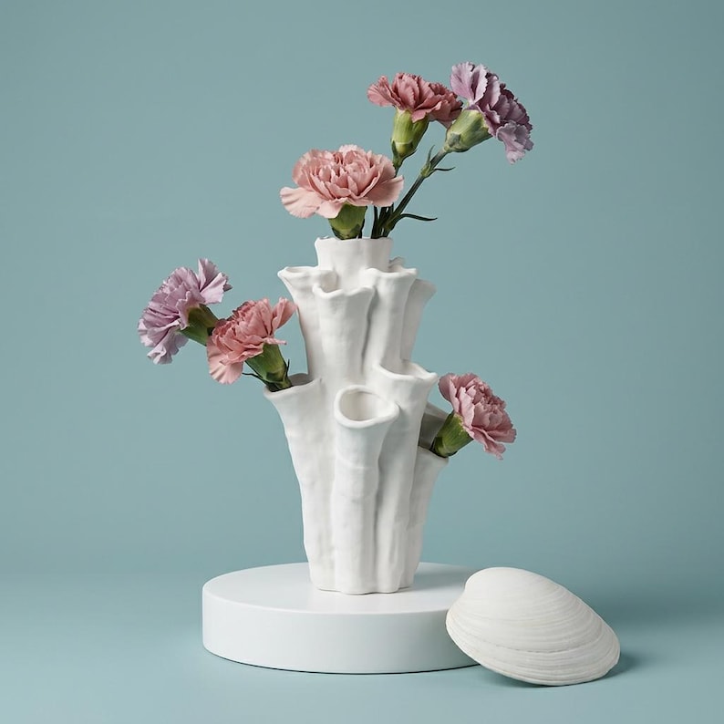 Matte white textured coral vase with branching openings holding pink carnations, with a white seashell beside it on a teal backdrop. A sculptural vase about 7.2 in tall and 3.9 in wide.