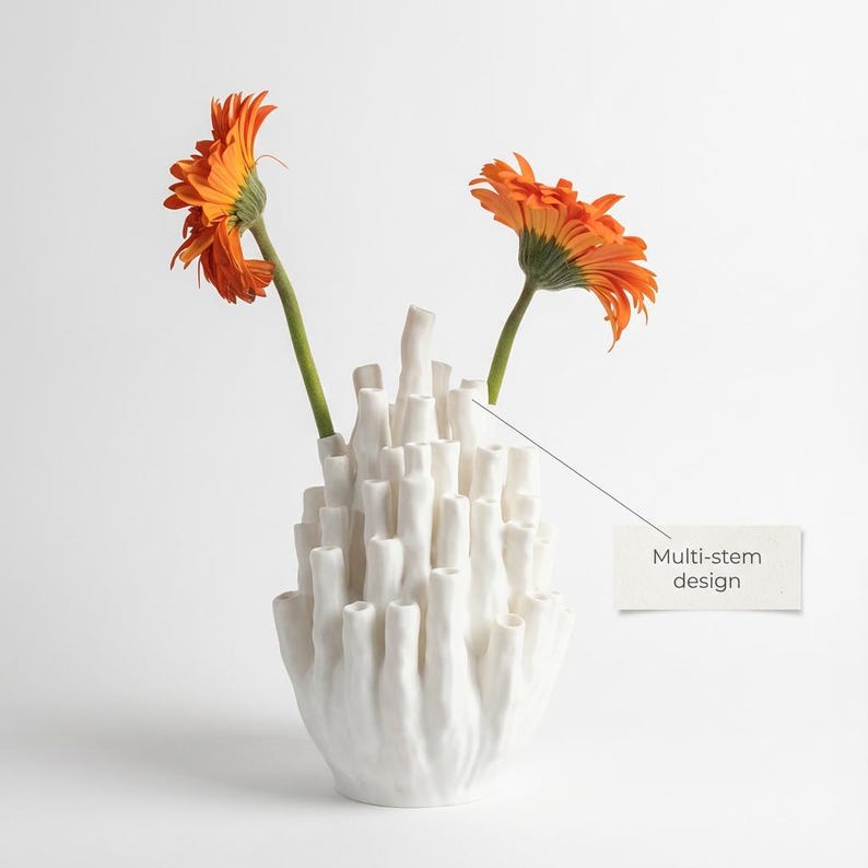 Matte white textured ikebana vase holding orange gerbera flowers on a light gray background, with a small text card beside it.
