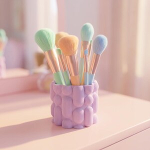 Textured matte lavender small vase holding pastel makeup brushes on a soft pink vanity in gentle light.