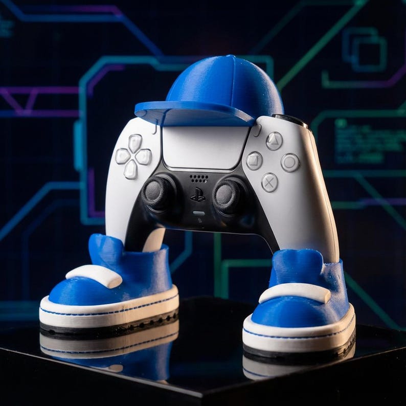 Controller holder with a matte blue baseball cap and blue and white sneakers holding a white and black controller upright against a dark background with a teal circuit pattern, great gaming room decor.