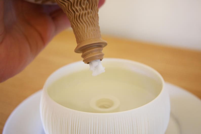 Angled view into a matte cream-white bowl of a self watering planter, with the brown cone-shaped core angled in from above, on a warm amber-brown background.