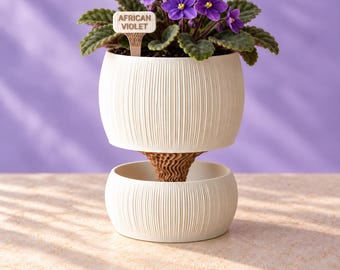 May include: An African violet plant with purple flowers and green leaves sits in a white, vertically ribbed, two-part self-watering planter. A small, light-colored plant marker with the text "AFRICAN VIOLET" is inserted into the soil.