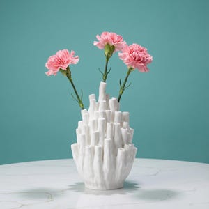 Matte white textured coral vase holding three pink carnations, set on a white surface against a teal background. Sculptural vase about 7.2 in tall, a gift for plant lover.