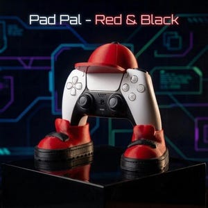 Controller holder with a matte red baseball cap and red and black sneakers holding a white controller on a dark circuit-pattern background, with the text "Pad Pal - Red & Black". A gaming room decor piece.