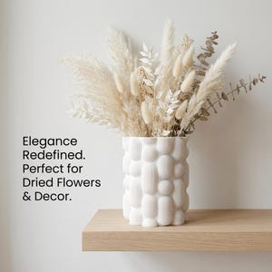 Textured matte white vase holding dried flowers on a light wood shelf, with the text "Elegance Redefined. Perfect for Dried Flowers & Decor." as a unique vase.
