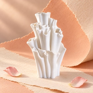May include: A white ceramic vase with a multi-tiered, organic structure resembling coral or ruffled flower petals. The object features several vertical, tubular openings of varying heights with wavy, scalloped edges and a smooth matte finish.