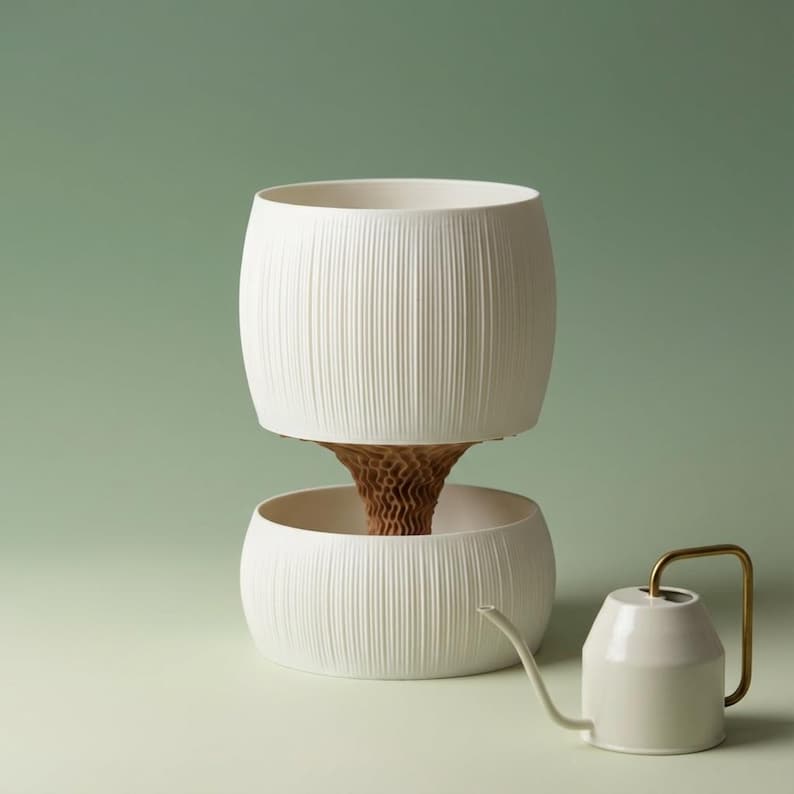 Textured matte white self watering planter, about 5 in wide and 7 in tall, with a ribbed upper pot nested over a lower bowl, on a sage green backdrop beside a small cream watering can.