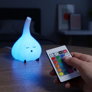 Blue glowing garlic lamp on a table while a hand holds a multicolor remote