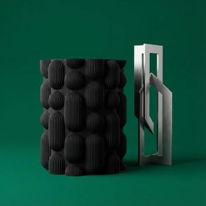 Textured matte black bubble vase beside a silver geometric sculpture on a deep green background.