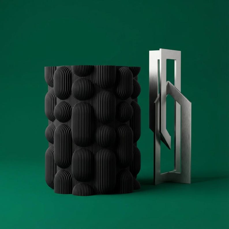 Textured matte black bubble vase beside a silver geometric sculpture on a deep green background.