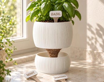 May include: A white two-tiered planter with a ribbed texture and a brown central support. A green basil plant grows in the top tier with a white label reading BASIL. Two additional white labels reading MINT and ROSEMARY lie nearby.