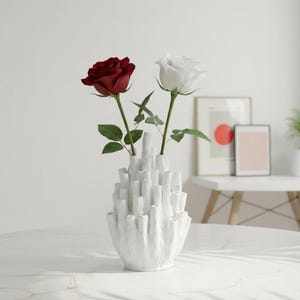 Matte white sculptural vase holding dark red flowers on a light gray surface with a minimal background.
