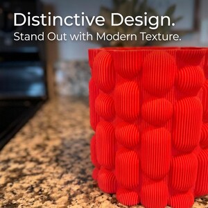 Close view of a textured matte red vase on a speckled brown kitchen counter, with the text "Distinctive Design. Stand Out with Modern Texture."