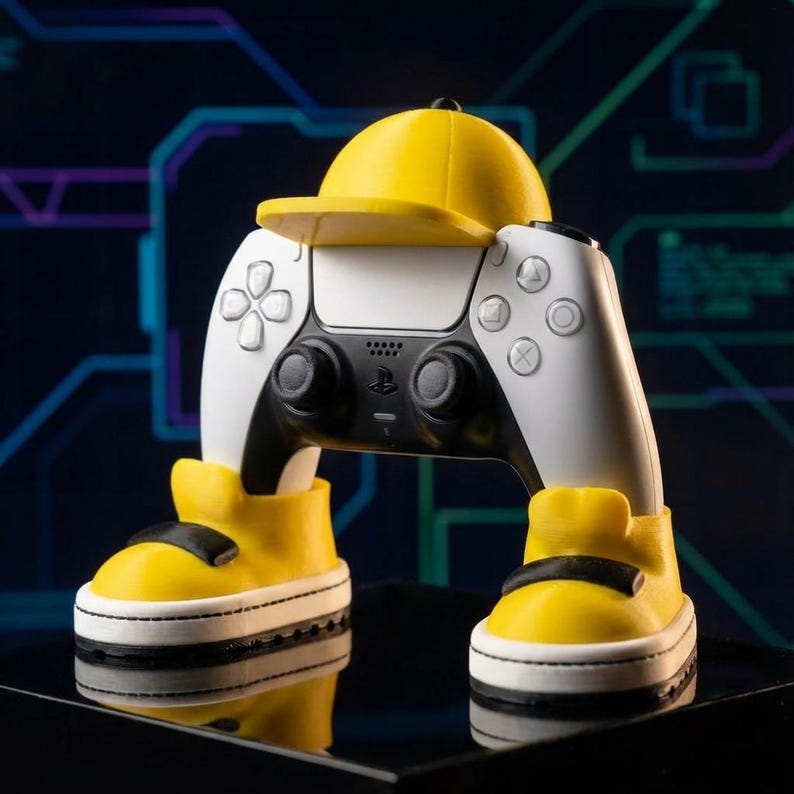 White controller holder with a matte yellow baseball cap and matching yellow sneakers holding a white and black controller on a dark surface with a faint blue circuit pattern, a fun controller holder.