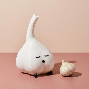 Unlit white garlic lamp next to a small real garlic bulb on a pink background