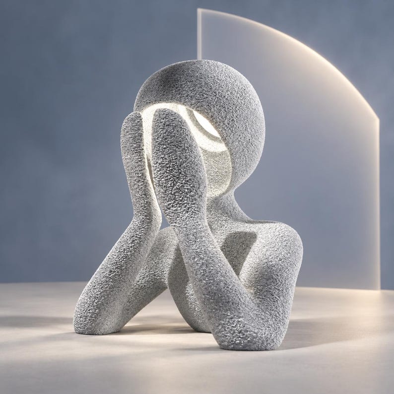 Abstract sculpture lamp, a seated figure resting its face in its hands, with a matte textured light gray surface and soft warm white glow, on a pale tabletop. Size is 8.9 inches tall, 8.3 wide and 5.2 deep.
