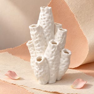 May include: A white ceramic vase with a textured, organic surface resembling coral. The structure consists of multiple vertical, tubular openings of varying heights clustered together, creating a complex, multi-stemmed silhouette with a matte finish.