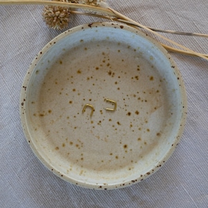May include: Two small gold hoop earrings on a speckled white ceramic dish.