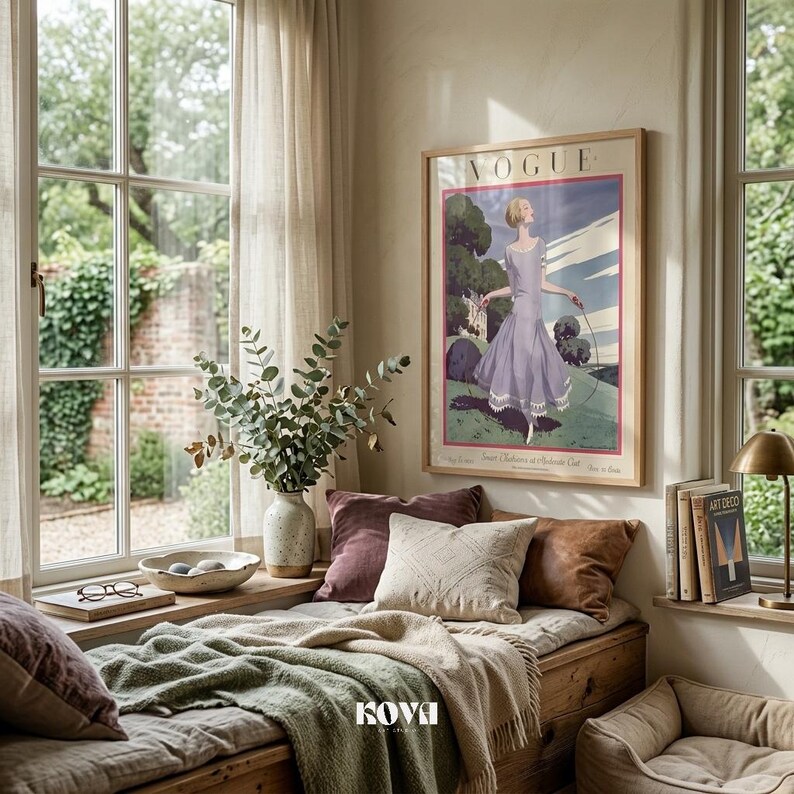 May include: A cozy window seat with a framed Vogue poster featuring a woman in a lavender dress. The scene includes decorative pillows, a green blanket, a vase with greenery, and a small lamp, creating a relaxing interior design.