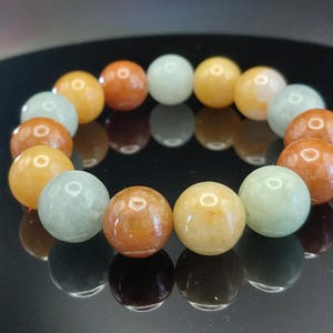 May include: A beaded bracelet featuring smooth, polished spherical beads in alternating shades of pale mint green, warm amber, and golden yellow. The beads are arranged in a circular pattern, showcasing a glossy, reflective surface finish.