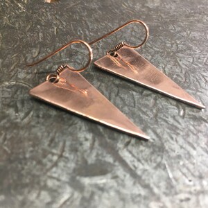 May include: A pair of copper triangle earrings with a hammered texture. The earrings have a simple wire hook closure.