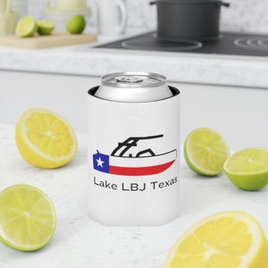 May include: White can cooler with a black and red Texas flag and a black silhouette of a boat. The text "Lake LBJ Texas" is printed below the flag.