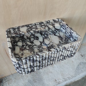 May include: A white and black marble sink with a unique ribbed design around the edge. The sink has a single drain hole in the center.