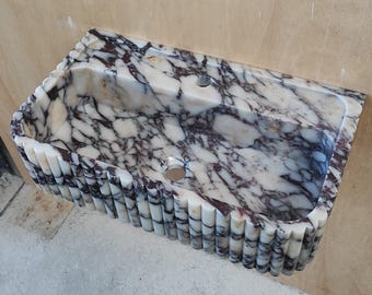 May include: A rectangular wall-mounted sink crafted from white marble with prominent dark purple veining. The exterior features a vertical fluted design along the front and sides, with a central drain hole and a faucet hole on the flat back ledge.