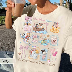 May include: Ivory-colored t-shirt featuring a collage of Disney characters and icons. The design includes Mickey and Minnie Mouse, Dumbo, and other characters in colorful frames. Text reads "Walt Disney World" and "The Most Magical Place on Earth."