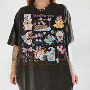 May include: Dark gray t-shirt featuring various Disney character illustrations within decorative frames. The shirt includes the text "Walt Disney World" and "The Most Magical Place on Earth". The design incorporates images of Mickey and Minnie Mouse, Dumbo, and other iconic Disney elements.