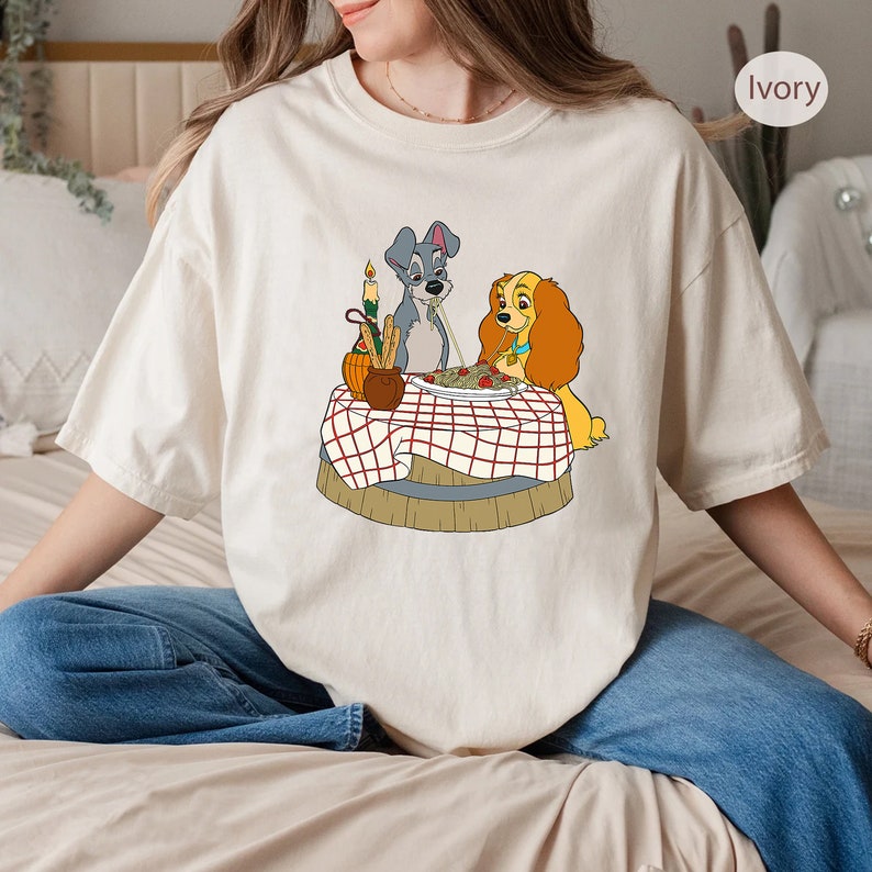 May include: A white t-shirt with a cartoon image of Lady and the Tramp sharing a plate of spaghetti. The image is in a vintage style and features a red and white checkered tablecloth.