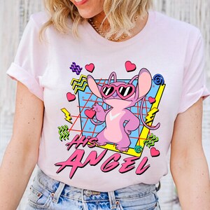 Peut inclure: T-shirt rose avec un personnage de dessin anim&eacute; portant des lunettes de soleil et le texte "His Angel" dans un style r&eacute;tro.