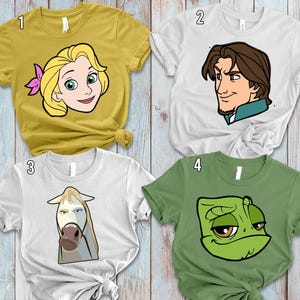 May include: Four graphic t-shirts featuring cartoon characters. The shirts are in various colors: mustard yellow, white, and green. The designs include a blonde woman, a man with brown hair, a white horse, and a green chameleon. The shirts are displayed on a wooden surface.