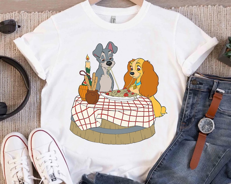 May include: White t-shirt with a cartoon image of Lady and the Tramp sharing a plate of spaghetti. The image is in a vintage style with a red and white checkered tablecloth.