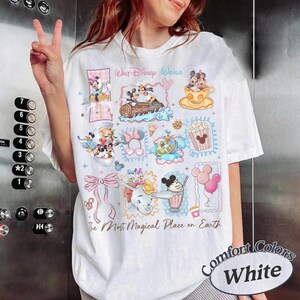 May include: White t-shirt with colorful Disney character graphics. Features Mickey and Minnie Mouse, Donald Duck, and Dumbo. Text includes "Walt Disney World" and "The Most Magical Place on Earth."