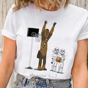 Op de afbeelding: Wit T-shirt met een cartoon illustratie van Chewbacca die basketbal speelt, een basketbalring en twee Stormtroopers. De tekst "Who invited him?" staat eronder.