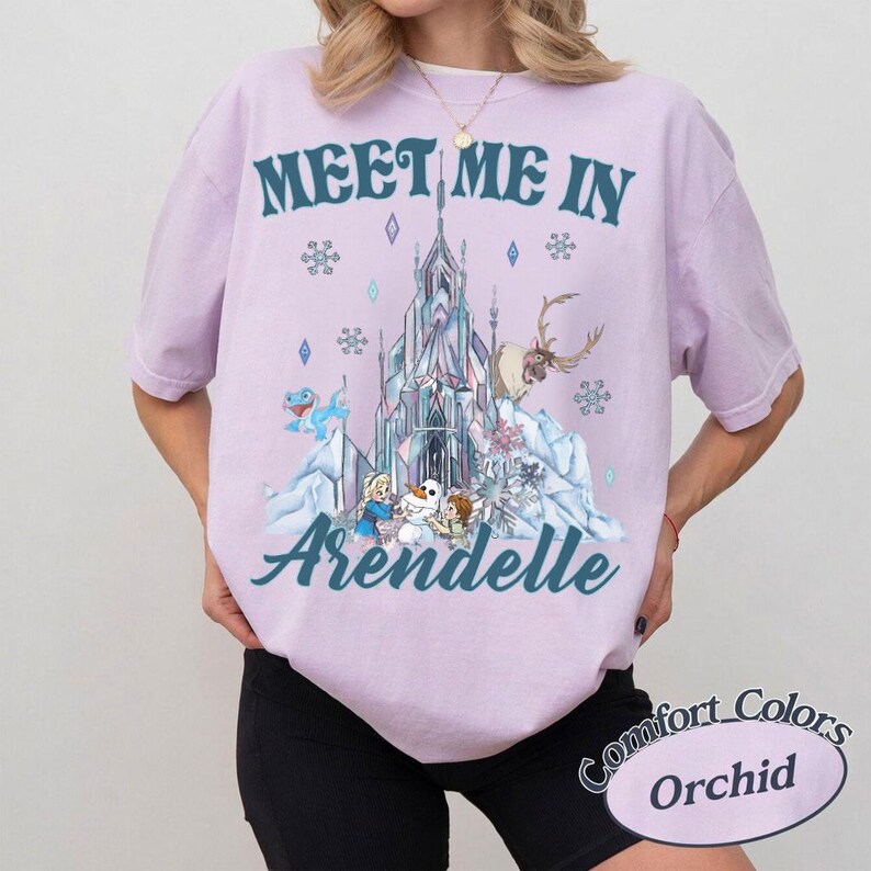 May include: Orchid-colored t-shirt with the text "Meet Me In Arendelle" above a graphic of a castle, characters, and snowflakes. The shirt is a Comfort Colors brand.
