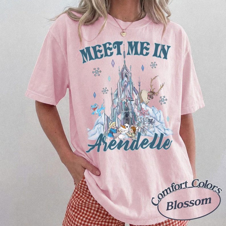 May include: Pink short-sleeved t-shirt with the text "Meet Me In Arendelle" above a graphic of a castle, characters, and snowflakes. The shirt also has the words "Comfort Colors Blossom" in a circle.