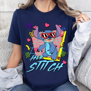 Peut inclure: Un t-shirt bleu marine avec un motif r&eacute;tro de Stitch de Lilo & Stitch portant des lunettes de soleil en forme de c&oelig;ur. Le motif comprend des accents roses, jaunes et bleus. Le texte "Her Stitch" est imprim&eacute; en gras et en style stylis&eacute; sous le motif.