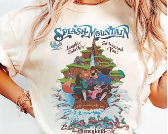 May include: A cream-colored t-shirt featuring a graphic of Splash Mountain with Br'er Rabbit, Br'er Fox, and Br'er Bear in a log flume. The text reads Splash Mountain, Laughin' Splashin' Satisfactual Fun!, and Disneyland in dark blue and brown.