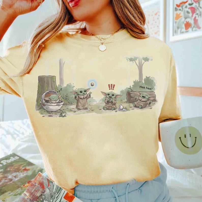 May include: Yellow t-shirt featuring a cartoon illustration of a character from a popular science fiction franchise. The graphic depicts the character in various poses with the text "Hee hee!" and other symbols.