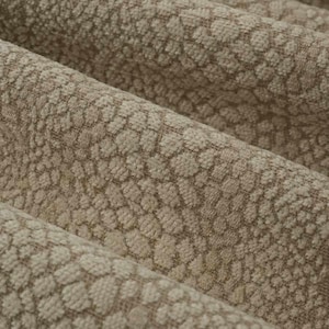 May include: Close-up of a beige fabric with a textured pattern of small, repeating shapes. The fabric has a subtle sheen and a soft, luxurious feel.