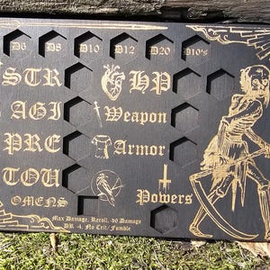 May include: Black wooden tabletop RPG game board with engraved gold lettering and illustrations. Features slots for dice and game stats like STR, AGI, and HP. Includes a skeleton graphic and text: Max Damage, Recall, de Damage, SR -4, Fz Crit/Fumble.
