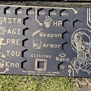 May include: A black wooden game board with etched gold-colored graphics and text. The board features various icons and words like "STR," "AGI," "Weapon," and "Armor." It has a futuristic, tech-inspired design, with a circuit board-like border.
