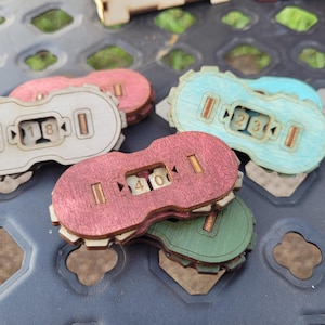 Peut inclure: Quatre compteurs de nombres en bois avec des teintes de couleurs différentes. Les compteurs sont numérotés 18, 40, 23 et 1. Les compteurs sont disposés en pile sur une surface noire.