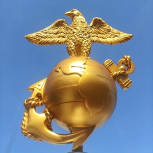 May include: A gold eagle perched atop a globe with an anchor, a symbol of the United States Marine Corps.