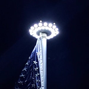 May include: A white flagpole with a ring of white LED lights at the top. A blue and white flag is hanging from the pole.