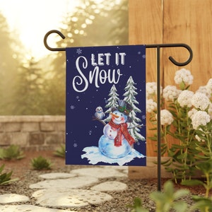 May include: A garden flag with a snowman design. The flag features a snowman wearing a top hat, scarf, and holding a branch with an owl. The words "LET IT SNOW" are written in white script on a navy blue background.