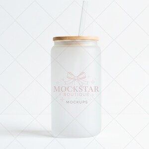 May include: A frosted glass can-shaped tumbler with a wooden lid and a clear straw. The tumbler has a pink logo that says "MOCKSTAR BOUTIQUE MOCKUPS". The background is a white diamond pattern.
