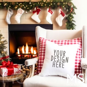 May include: White throw pillow with the text "YOUR DESIGN HERE" on a white armchair with a red and white checkered pillow in front of a fireplace with a lit fire and Christmas stockings hanging above.